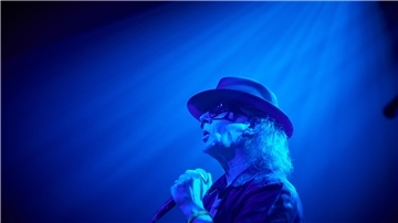 Ein Sänger, der wie Udo Lindenberg aussieht, steht auf einer Bühne, die in blaues Scheinwerferlicht getaucht ist.