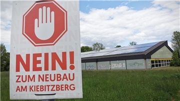 Das Foto zeigt links ein Schild mit der Aufschrift "Nein zum Neubau am Kiebitzberg" und rechts die Tennishalle des SV Nordenham.