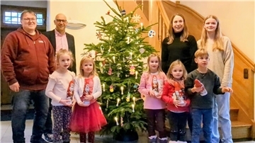Kinder und Erwachsene stehen vor einem geschmückten Weihnachtsbaum. 