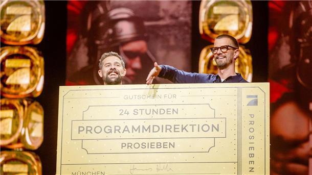 Was Joko und Klaas an ihrem TV-Sonntag so planen Klaas Heufer-Umlauf (l) und Joko Winterscheidt hinter einem Schild mit der Aufschrift „Gutschein für 24 Stunden Programmdirektion ProSieben“.