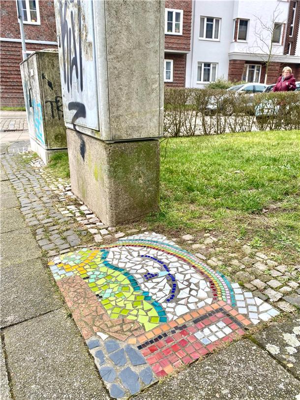 Kleines buntes Mosaik zwischen grauen Pflastersteinen mitten in Bremerhaven: Am Waldemar-Becké-Platz hat wohl irgendwer aus den Wohnhäusern ringsum in den Boden ein leuchtendes Regenbogen-Bild gezaubert.