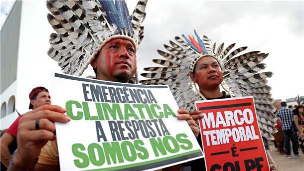 Brasilien: Gesetzesinitiative könnte Indigene benachteiligen „Klima-Notstand - die Antwort sind wir“ steht auf dem Plakat (r) eines indigenen Demonstranten, der in Brasilia gegen den Gesetzesentwurf zur Ausweisung von Schutzgebieten protestiert.