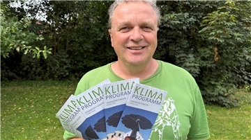 Mann in einem grünen T-Shirt mit Flyern in der Hand.