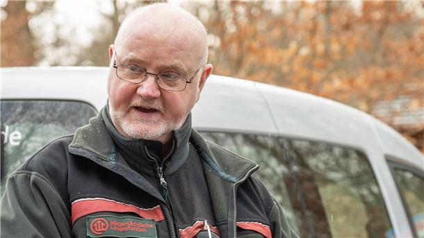 Ein Mann mit Brille steht im Wald vor einem Auto