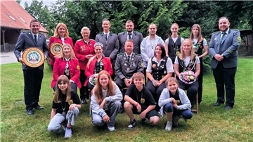 Menschen stehen zu einem Gruppenbild aufgereiht auf einer Grasfläche. 