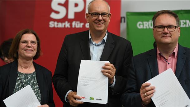 Kristina Vogt (Linke,), Andreas Bovenschulte (SPD) und Björn Fecker (Bündnis 90/Die Grünen) halten den Koalitionsvertrag in der Hand. 