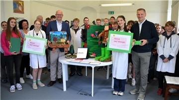 Schüler und Politiker stehen gemeinsam um einen Tisch herum. Schüler des NIG haben für Politiker kreative "Heilmittel" entwickelt. 