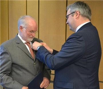 Landrat Marco Prietz steckt Wolfgang Dörfler im Sitzungssaal des Kreishauses das Verdienstkreuz unter das Revers.
