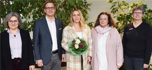 Vier Frauen und ein Mann stehen nebeneinander. Die Frau in der Mitte hält einen Blumenstrauß in einer Hand.