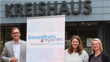 Drei Leute und ein Aufsteller vor dem Kreishaus in Brake