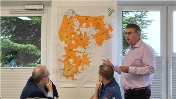 Drei Männer vor einer Karte des Landkreises Cuxhaven auf der orangefarbene Flächen und grüne Punkte eingezeichnet sind.