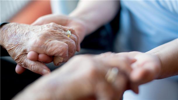 Die Hände einer jüngeren Person halten die Hände einer älteren Person