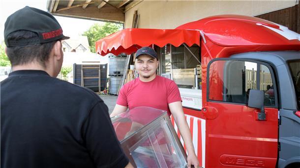 Zwei Männer tragen eine Kühlvitrine zu einem roten Foodtruck