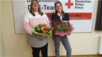 Maren Wacker und Nicole Krentzel stehen lächelnd vor einem Transparent des DRK Tarmstedt und halten Blumensträuße in den Händen.