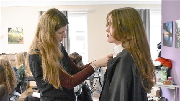 Zwei Mädchen mit langen Haaren stehen nebeneinander und befestigen etwas an einem Kragen.