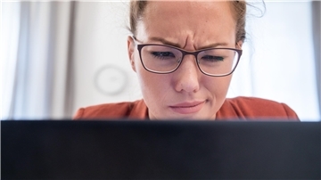 Eine Frau schaut mit skeptischem Blick auf den Bildschirm ihres Notebooks. 
