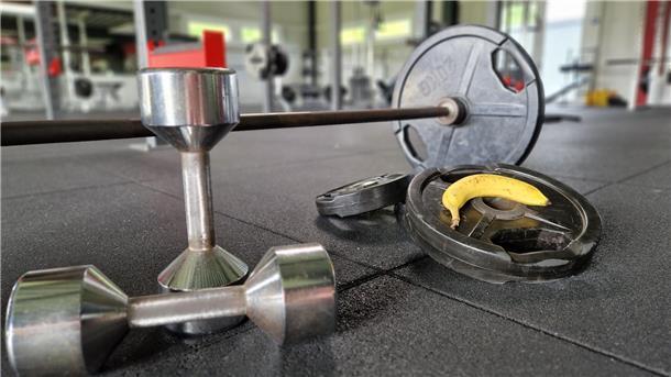 Bananen-Power: Dein schneller Energiekick vor dem Sport Eine Banane mit Hantelstange, Gewichtsscheiben und Kurzhanteln.