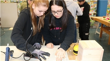 Zwei Schülerinnen arbeiten handwerklich. Im Hintergrund arbeitet eine Gruppe von Schülern.