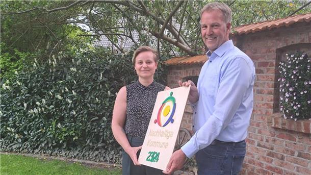 Luisa Wolter von der Kommunalen Umwelt-Aktion überreicht Beverstedts Bürgermeister Guido Dieckmann (parteilos) im Garten der Gaststätte Büttelmann in Wollingst die Auszeichnung als Nachhaltige Kommune. 