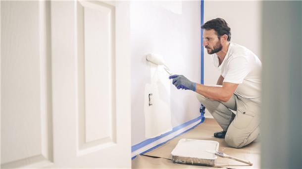 Ein Maler und Lackierer streicht eine Wand weiß.