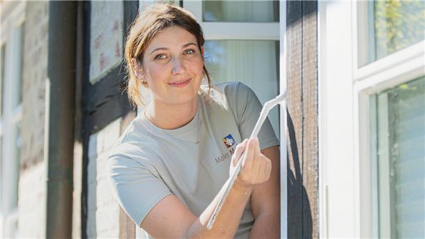 Malin Backhaus streicht mit einem Pinsel Fensterrahmen an 