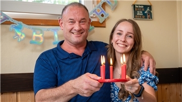 Jeffrey Bettez und Malin Fleischauer halten einen Geburtstagskranz mit fünf brennenden Kerzen in der Hand.