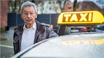 Ein Mann steht vor einem Taxi. 