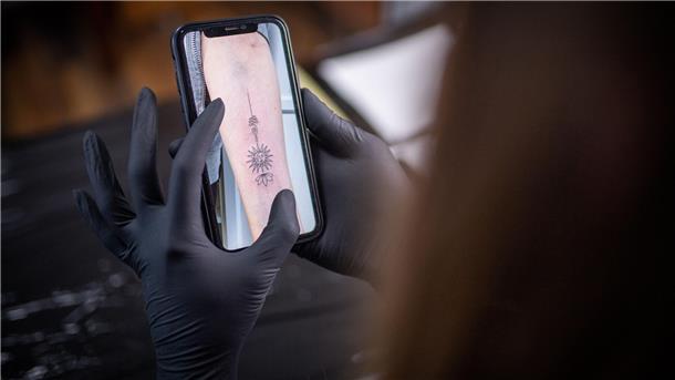 Diese junge Frau findet im Tattoo-Studio auf dem Dorf ihre Bestimmung Auf dem Display eines Handys ist ein Tattoo Motiv zu sehen.