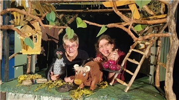 Zwei Frauen in der Kulisse eines Puppenspiels mit Puppen einer Kuh und einer Krähe