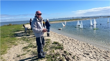 Leute stehen am Strand und navigieren ihre Modellsegelboote per Fernsteuerung