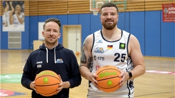 Zwei Männer stehen auf einem Basketballfeld und halten einen Basketball. 