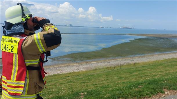 Ein Feuerwehrmann steht mit einem Fernglas auf dem deich