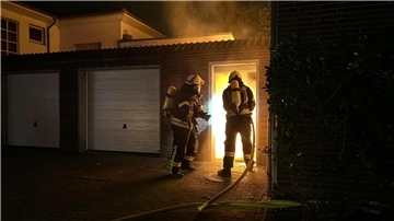 Einsatzkräfte der Feuerwehr löschen Brand zwischen Haus und Garagen