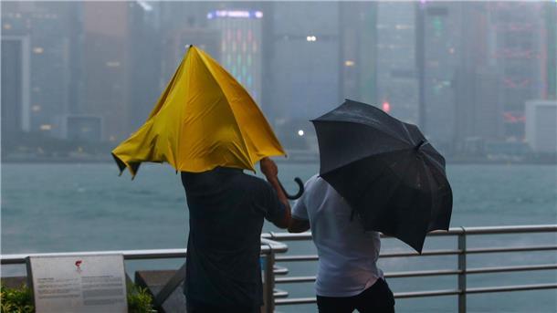 Menschen mit Regenschirmen kämpfen in Hongkong mit starkem Wind und Regen des Taifuns „Saola“.