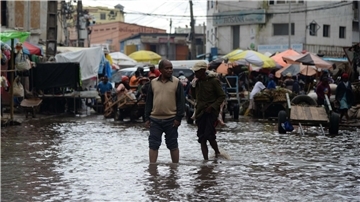 Menschen waten durch das Hochwasser einer überfluteten Straße in Antananarivo.