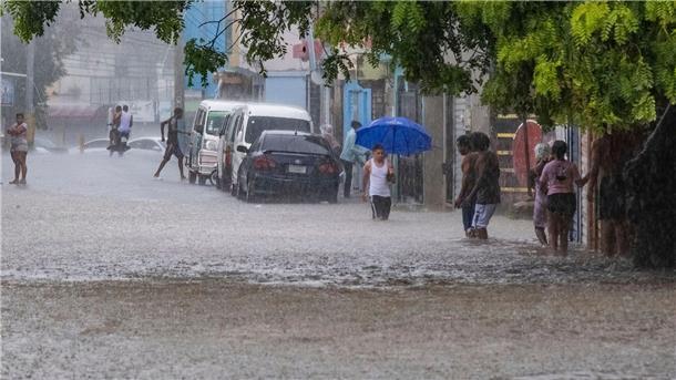 Menschen waten in Santo Domingo durch knietiefes Wasser auf einer Straße, die von den Regenfällen überflutet wurde.