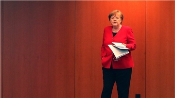Angela Merkel mit einer Hand in der Hosentasche und in der anderen Hand Papier.