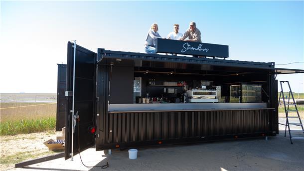 Michaela, Leonard und John Reinhardt testen den Sitz der gerade installierten „Strandhus“-Aufschrift auf dem Dach des Cafébar-Containers am Strand von Wremen.