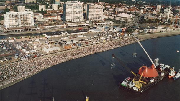 Legendäres Scorpions-Konzert in Bremerhaven: Hier gibt’s den kompletten Auftritt Massen drängen sich an einen Deich. Auf einem Fluss ist eine Bühne zu sehen.