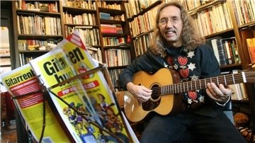 Ein langhaariger Mann spielt mit einem Buch auf einem Notenständer vor sich Gitarre. Peter Bursch ist der Gitarrenlehrer der Nation. 