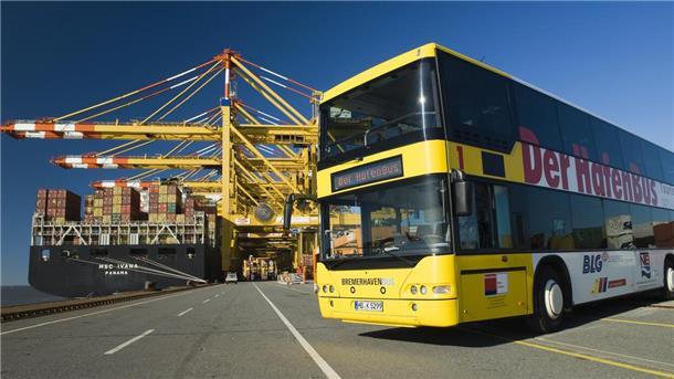Was kann man in Bremerhaven machen? Tipps für den Besuch in der Stadt am Meer Ein gelber Doppeldecker Bus steht vor einem Containerschiff im Hafen. Die Sonne scheint.