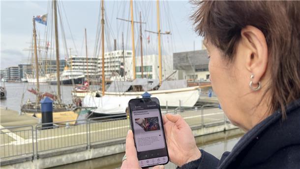 Forscher auf Zeit mit dem BremerhavenGuide Eine Frau steht im Hafengebiet und schaut auf das Display ihres Smartphones.