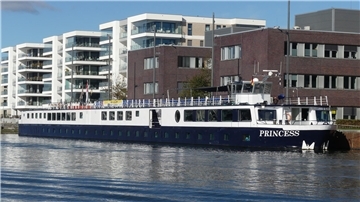 Das Flusskreuzfahrtschiff „Princess“ liegt am Kai in Bremerhaven. Im Hintergrund moderne Wohn- und Bürogebäude, das Schiff spiegelt sich im Wasser.