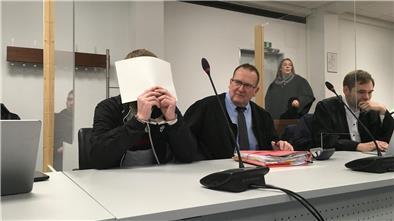 Angeklagter, der sich ein Blatt Papier vor das Gesicht hält.