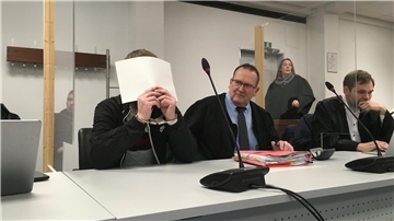 Angeklagter, der sich ein Blatt Papier vor das Gesicht hält.