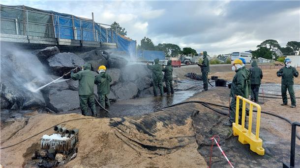Mit Hochdruckreinigern und in Schutzkleidung reinigen Kursteilnehmer eine Felsformation von Öl. Im Trainingszentrum im französischen Brest können sie mit echtem Öl üben.