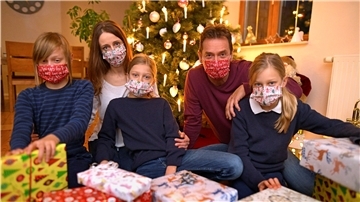 Eine Familie mit drei Kindern sitzt mit Mund-Nasen-Maske vor einem Weihnachtsbaum. 