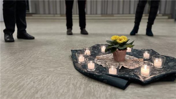 Auf einer grünen Decke stehen neun brennende Teelichter um eine gelbe Blume herum.