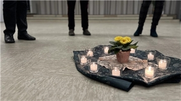 Auf einer grünen Decke stehen neun brennende Teelichter um eine gelbe Blume herum.