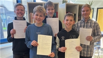 Fünf Jungen stehen lächelnd nebeneinander und halten Zettel in den Händen. 
